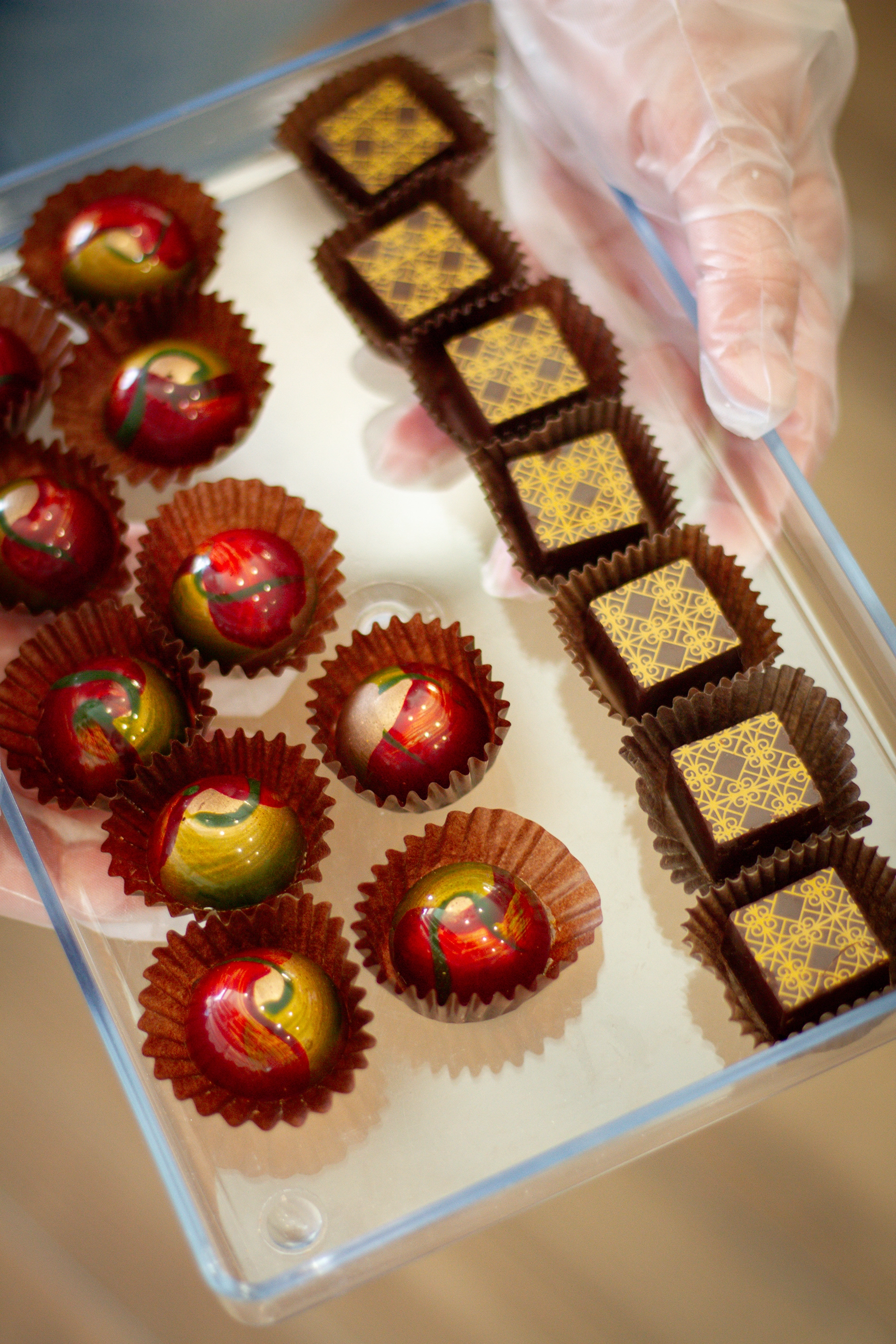 a worker holds a tray of shiny artfully crafted chocolate truffles