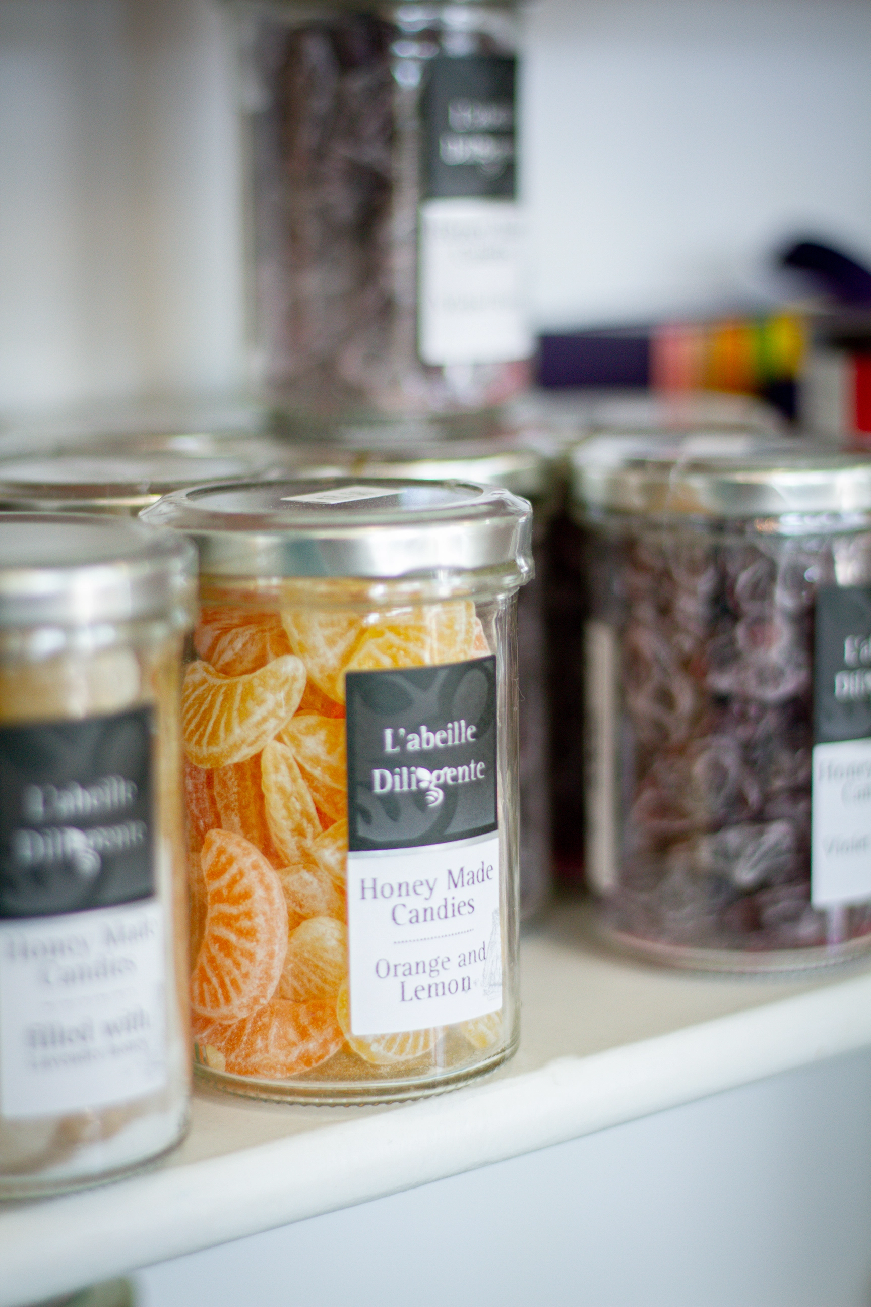 jars of hard sugar candy sit on a shelf, in focus is a jar of honey made orange and lemon candies