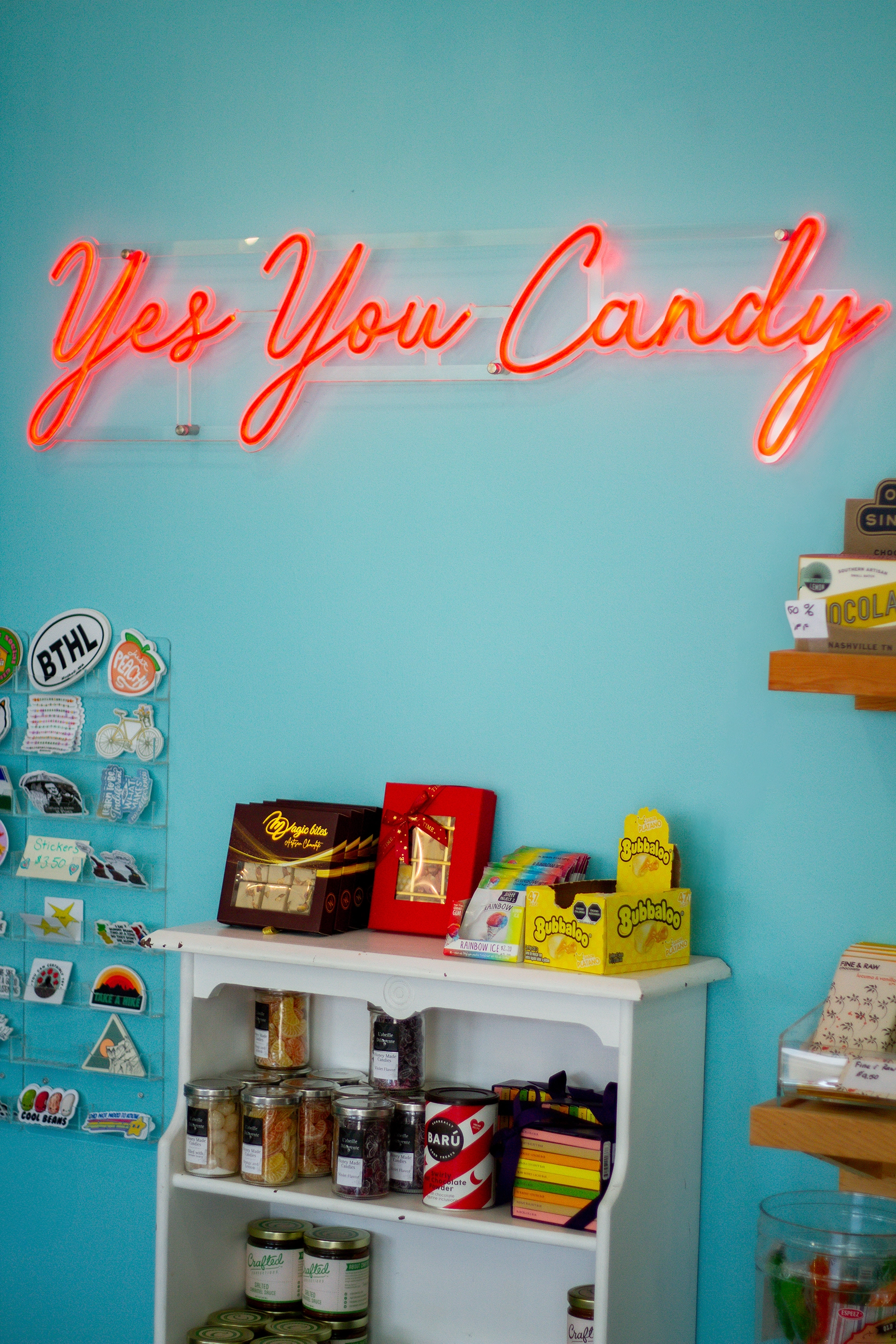 A colorful display of assorted gummy candies with a acrylic neon sign that reads "yes you candy"